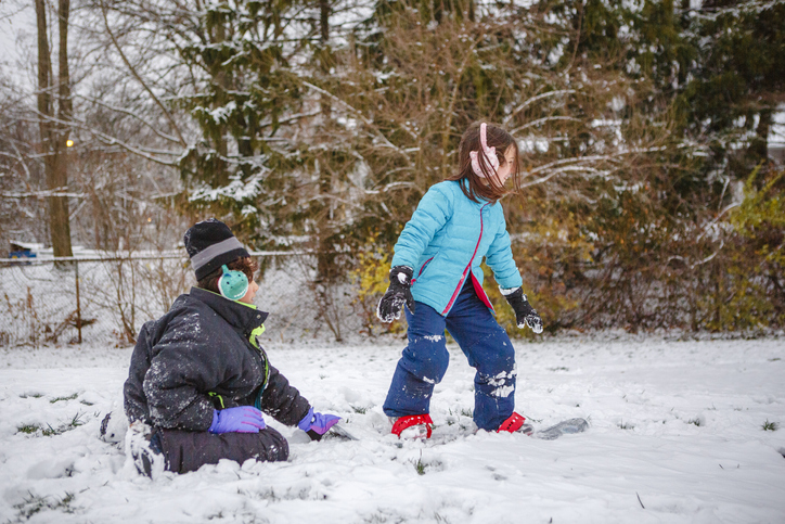 A boy teaches his little sister how to snowboard in winter