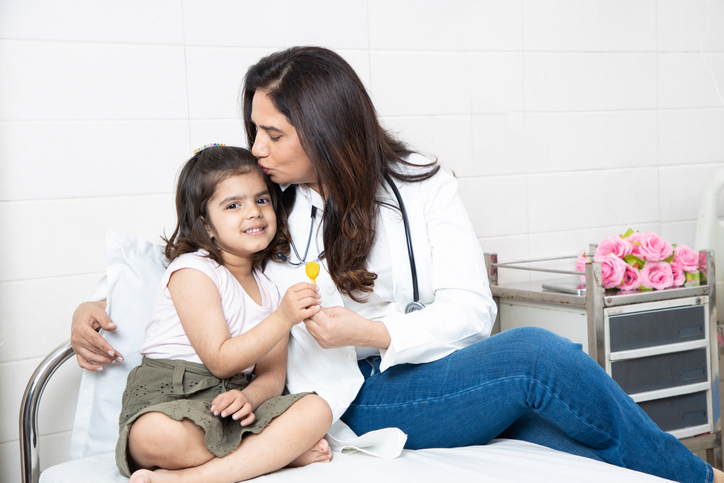 Happy little indian girl get lollipop from female doctor at meeting in hospital. Smiling child patient celebrating successful treatment finish with general practitioner at checkup in clinic.