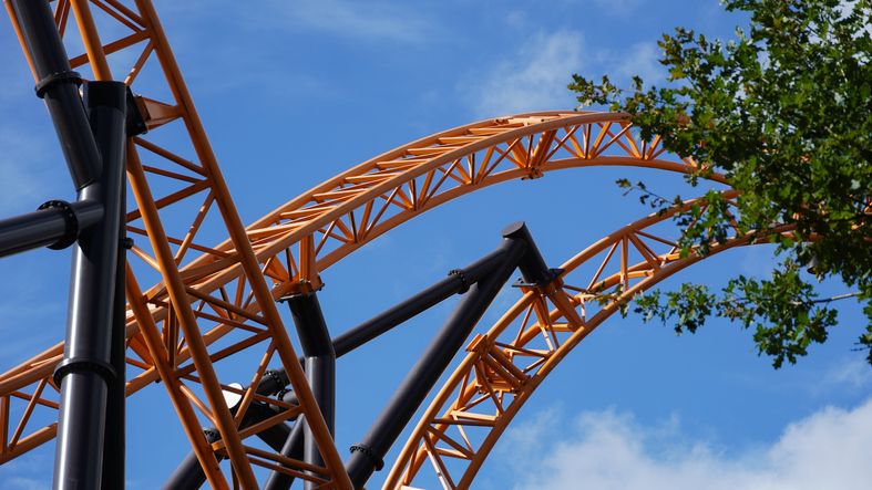 Orange-coloured roller coaster tracks of an extreme roller coaster, crossing under a blue sk