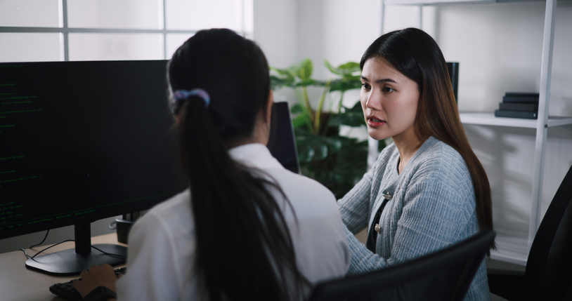 Asian female software developer explaining work to her colleagues at desk in an office.