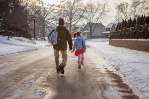 Rear-view of father and daughter walking to school on snowy street