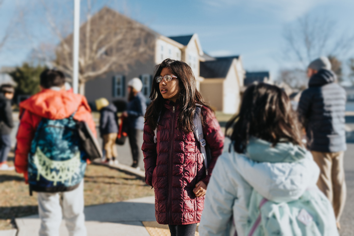 Children waiting at neighborhood school bus stop with their parents
