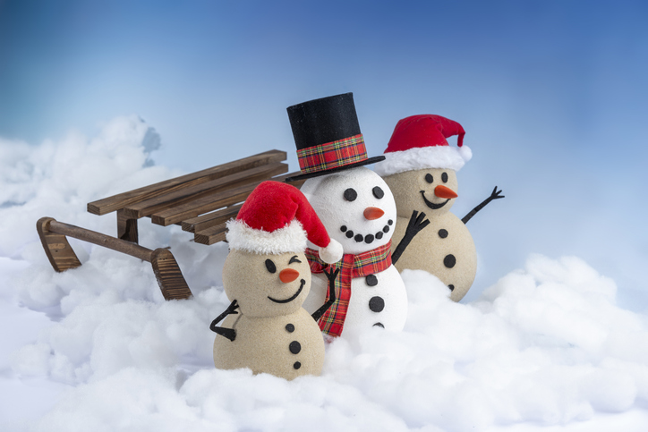 Snowman and two sandy snowmen pose together on a sled for a Christmas and New Year celebration