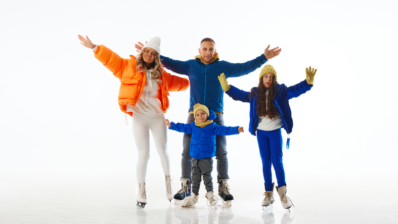 Family spread their arms wide, embracing fun of family time on ice, highlighting their playful spirit against white studio background.