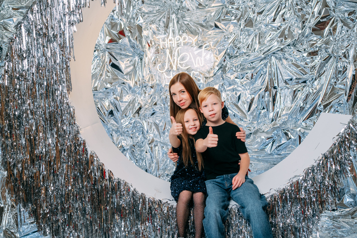 Happy family gesturing thumbs up while celebrating new year's eve together in a shiny silver photo booth