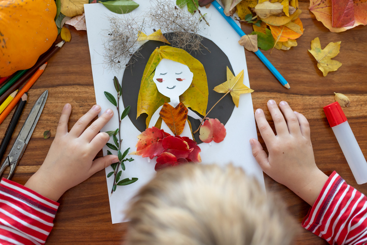Sweet child, boy, applying leaves using glue while doing arts and crafts at home