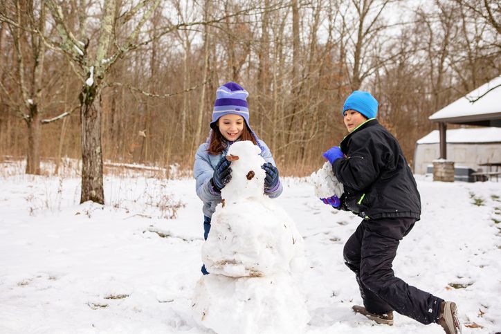 Two happy children build snowman together in winter