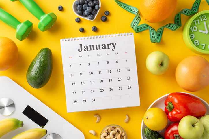 A January calendar surrounded by fresh fruits, vegetables, and fitness items, symbolizing a healthy start to the new year and balanced diet concept