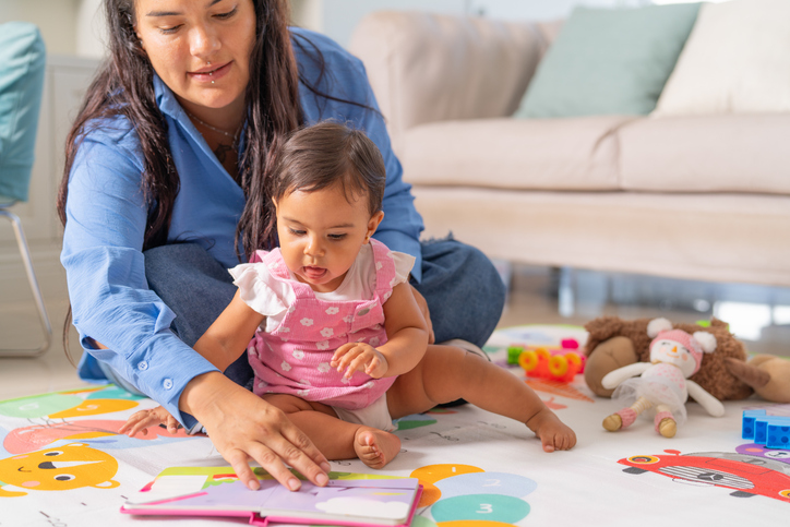 Mother reading a book to her baby daughter at home