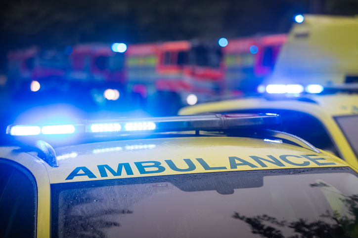 Close-Up Of Blue Light Flasher On Roof Of Ambulance Car Of Emergency Service Against Fire Engines.