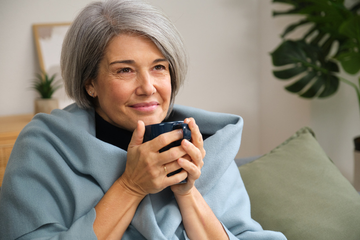 Serene mature woman enjoying a hot drink at home wrapped in cozy blanket