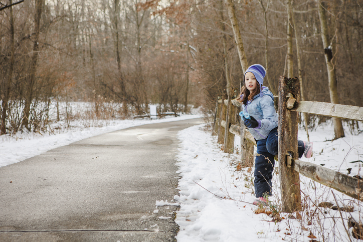 A little girl sits on wood fence along snowy fence with binoculars