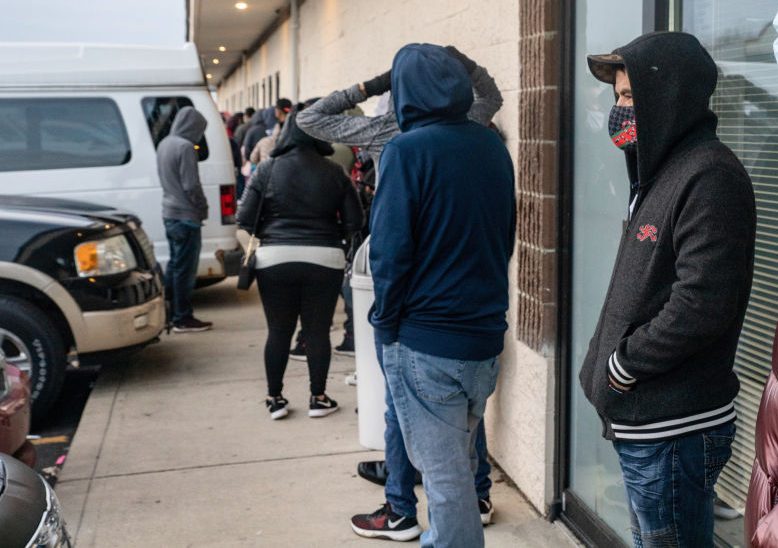 People wearing face masks wait in a line to finish the...