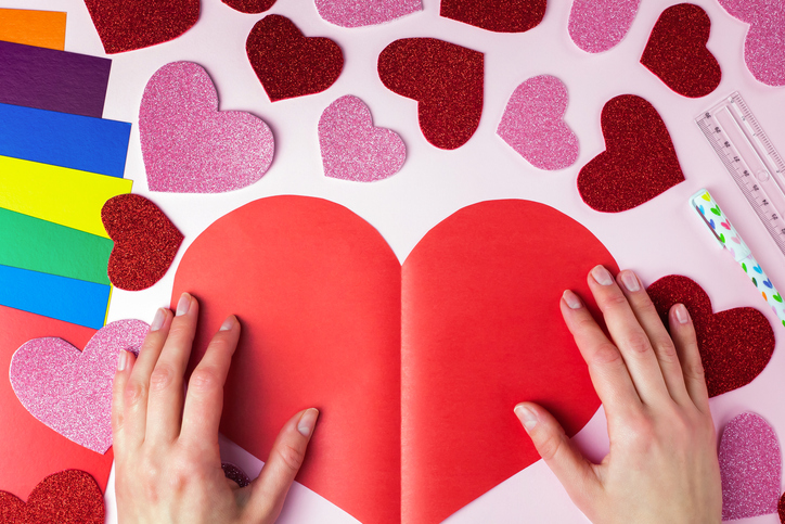 Woman's hands holds a big red paper heart. DIY concept for Valentine's day card crafts. Top view. Flat lay. Step by step photo instruction. Step 8.