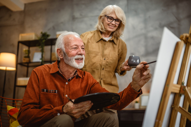senior man with his wife painting on canvas with a brush and palette