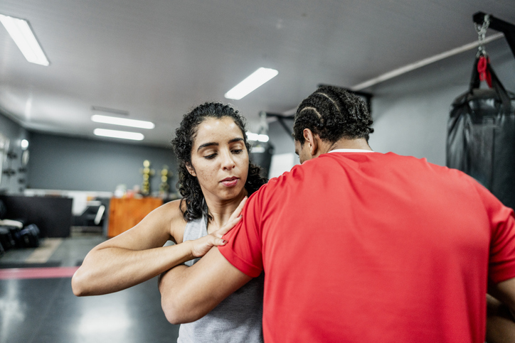 Mid adult woman practicing boxe self-defense with instructor at gym