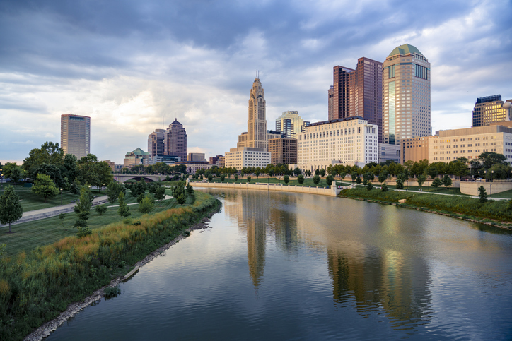 Scenic view of downtown Columbus, Ohio, during a calm evening with soft lighting, the skyline with modern skyscrapers and historic buildings reflecting in the Scioto River in the foreground