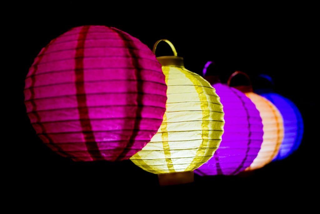 lighted paper lanterns in various colors hanging in the dark