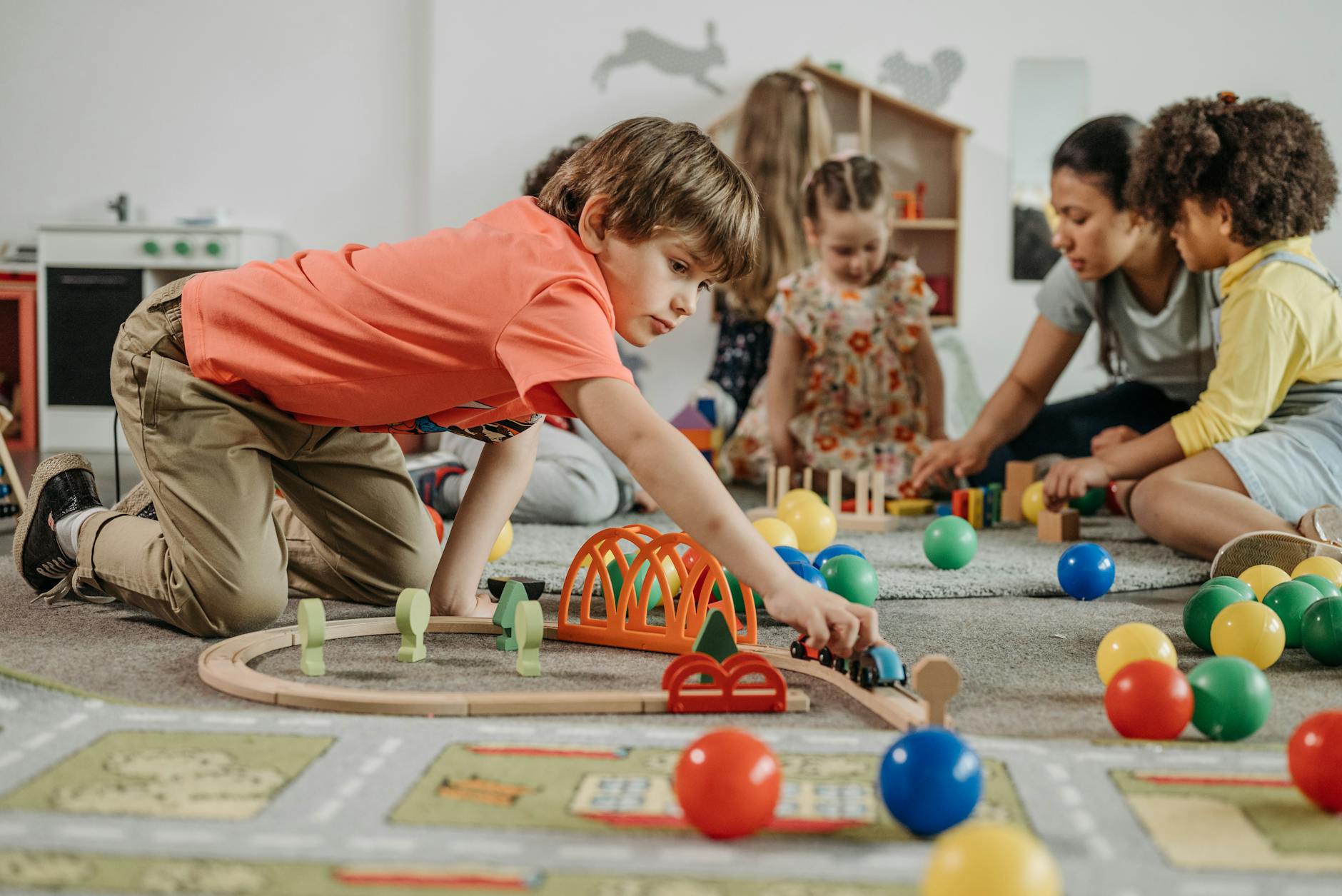 boy in orange shirt playing train toy on the floor