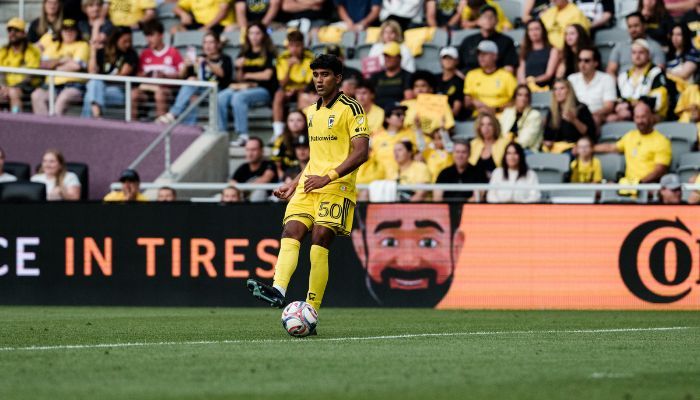 A soccer player in a yellow jersey dribbling the ball on a soccer field in front of a crowd of spectators.