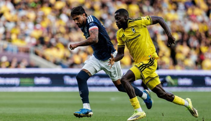 Two soccer players in action, one in a yellow jersey and one in a blue jersey, competing for the ball on a soccer field.