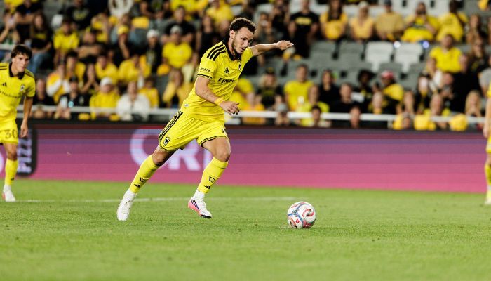 A soccer player in a yellow jersey dribbling the ball on a soccer field with spectators in the background.