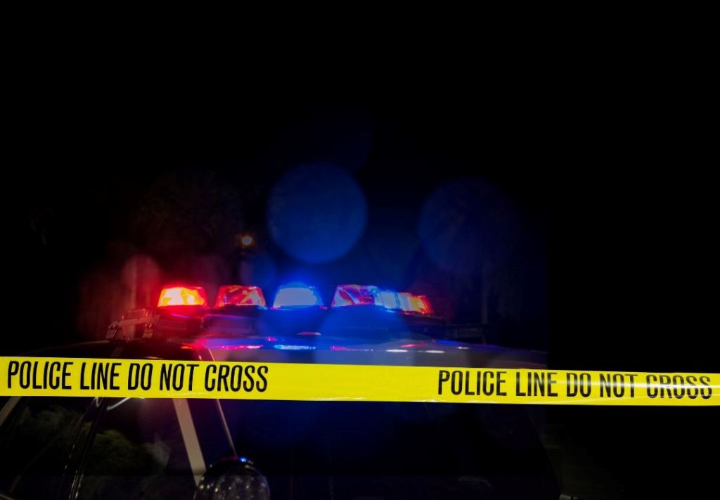 Police line do not cross tape at night with emergency vehicle lights in the background.