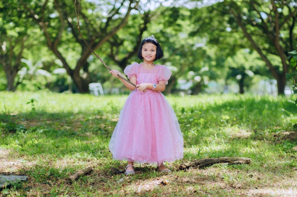 young girl in pink dress holding stick outdoors
