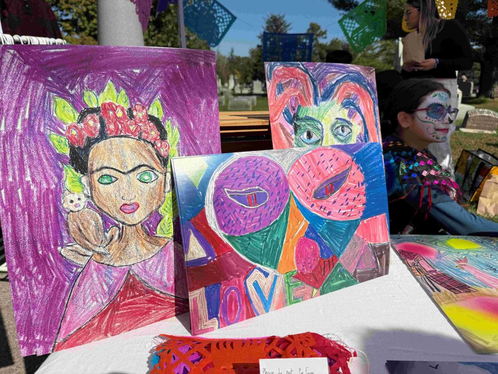 Colorful paintings and artwork displayed on a table, including a portrait of a woman with a floral crown and abstract designs.