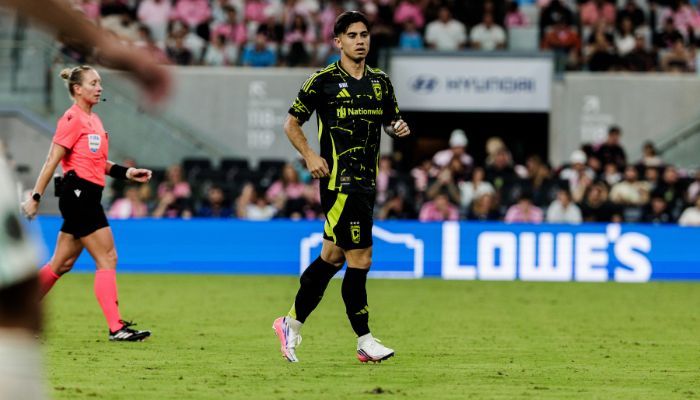 A soccer player in a black and yellow uniform running on a field during a match, with a Lowe's logo visible in the background.