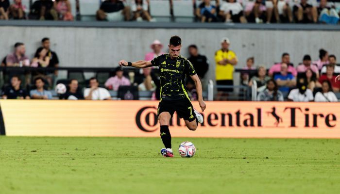 A soccer player in a black jersey dribbling the ball on a field, with a Continental Tire advertisement visible in the background.