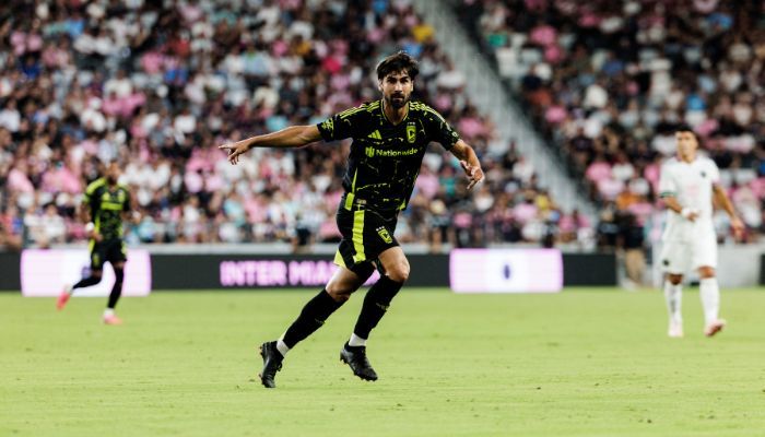 A soccer player in a green and black jersey running on a field during a match.