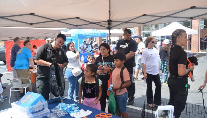 A crowd of people gathered at an outdoor event, with tents, tables, and police officers present.