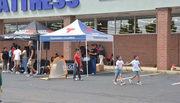 Outdoor event with tents, people, and a Telemundo Columbus logo visible.
