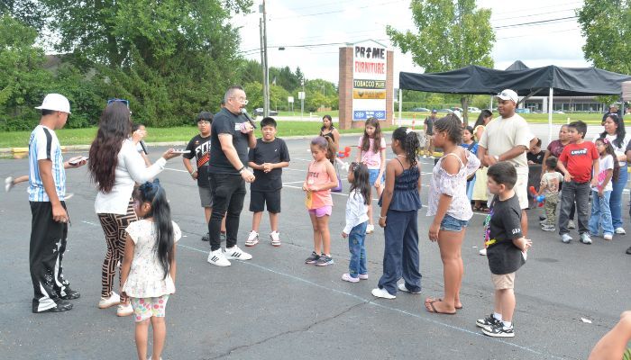 A group of people, mostly children, gathered in an outdoor setting with a tent and signage for "Prime Growers".