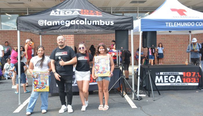 A group of people standing in front of a tent with the text "@lamegacolumbus" and a Telemundo logo.