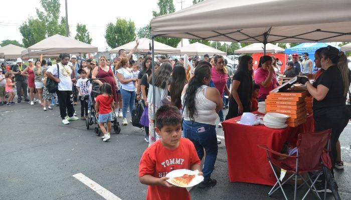 Crowded outdoor market with people in line at food vendor tents, a young boy holding a plate of food in the foreground.