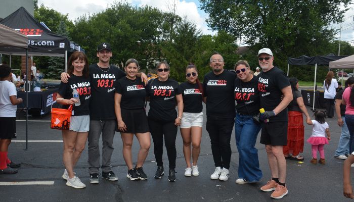 A group of people wearing black t-shirts with "La Mega 103.7" printed on them, standing together outdoors.