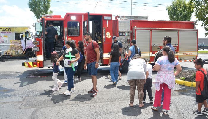 A group of people gathered around a red fire truck, with some people entering or exiting the vehicle.