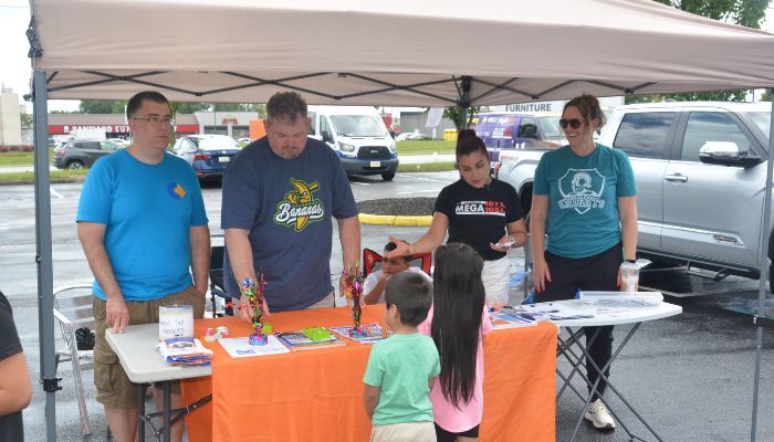 A group of people, including children, gathered at an outdoor booth selling various items and engaging with the public.