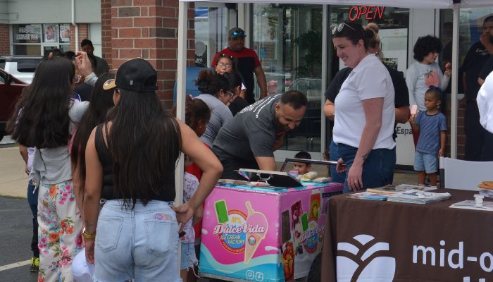A group of people gathered around a table selling various items, including a large pink box labeled "Takealida".
