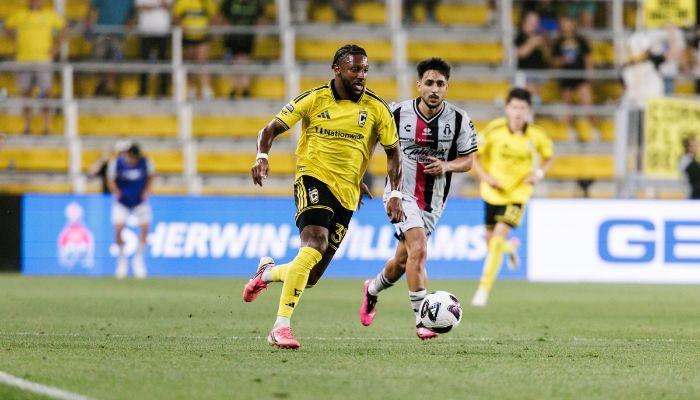 Two soccer players in yellow and white jerseys running on a field, one player dribbling the ball.
