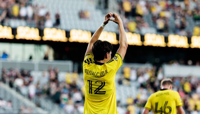 A soccer player in a yellow jersey with the number 12 on the back raises his arms in celebration on a soccer field.