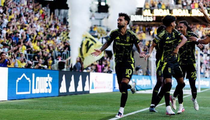 Soccer players celebrating a goal on the field in front of a cheering crowd.