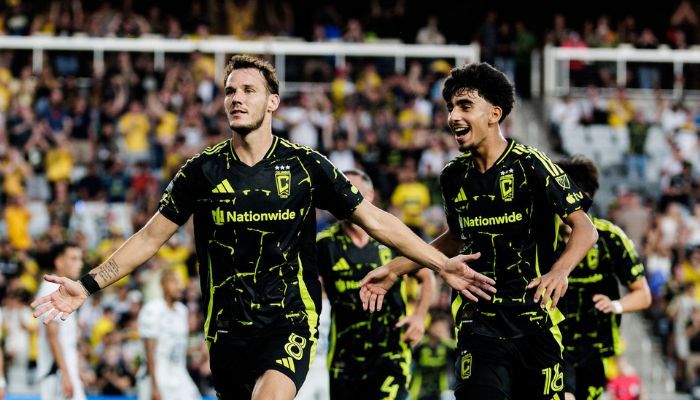 Two soccer players in black and green uniforms celebrating a goal on the field.