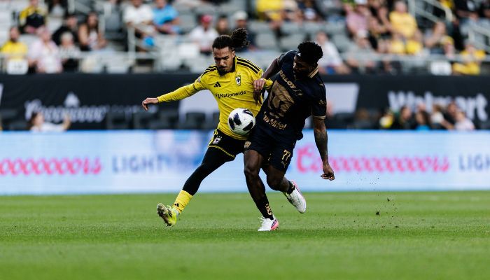Two soccer players competing for the ball on a soccer field, one wearing a yellow jersey and the other a dark jersey.