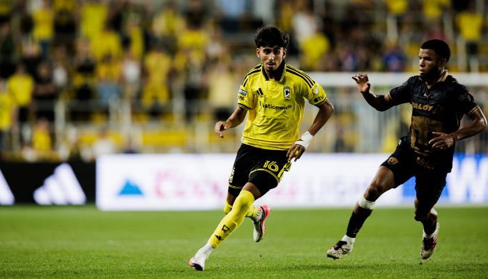 Two soccer players in yellow and black uniforms running on a soccer field.