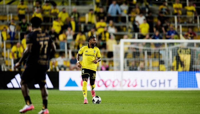 A soccer player in a yellow jersey dribbling the ball on a soccer field with spectators in the background.