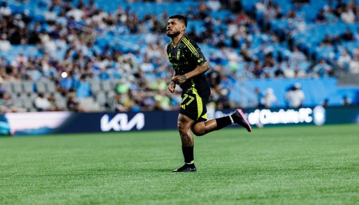 A soccer player in a yellow jersey running on a soccer field in a stadium with spectators in the background.