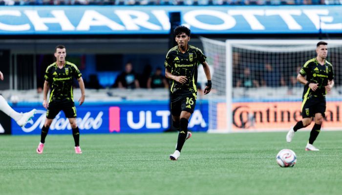 Soccer players in green uniforms running on a field with "Charlotte" signage visible.